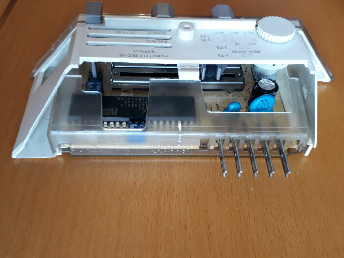Termostatens inre kretskort och komponenter, avmonterat, på ett träbord.
