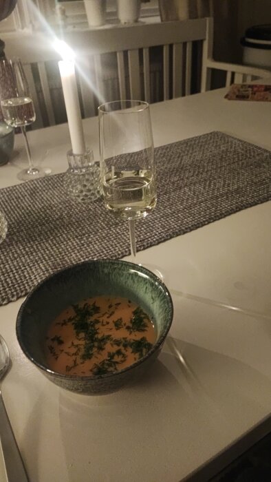 Mysig middagsscen med soppa, vinglas och levande ljus på ett bord.