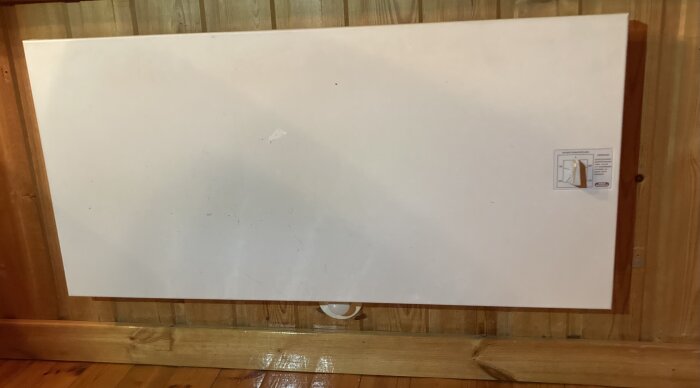 En stor vit tavla på en vägg omgiven av ett träram, med vissa märken och en pappersbit.