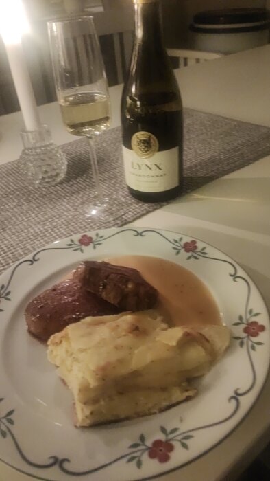 Middag med stek, potatisgratäng, sås och ett glas vin på ett bord.