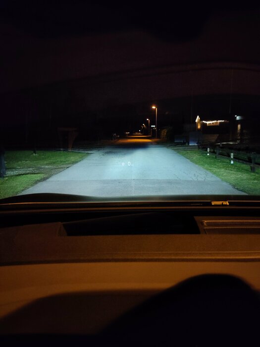 Mörk kvällsbild tagen från bilens förarsäte med utsikt över en öde gata upplyst av gatlyktor.