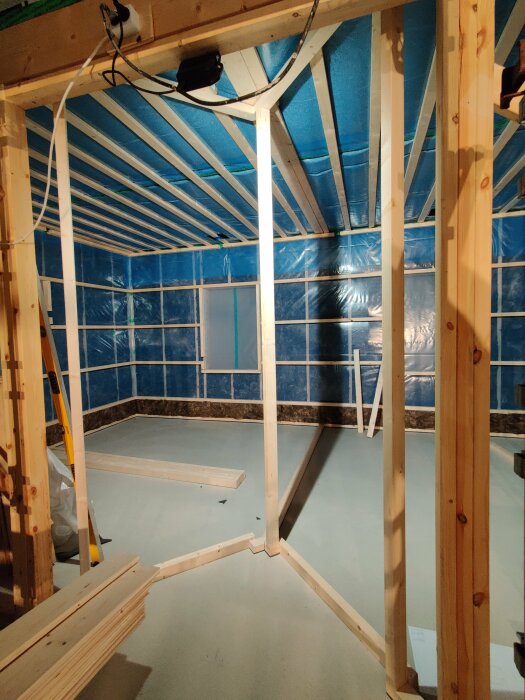 Oisolerat rum under konstruktion med träreglar, blå isoleringsmattor och plastfolie. Renoveringsprojekt eller nybyggnation.