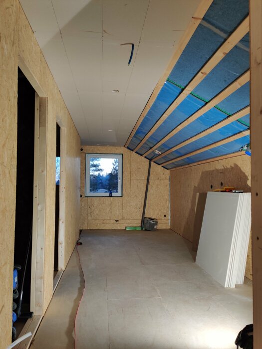 Pågående inomhusbygge, isolering synlig, spånskivor, ofärdigt tak, fönster, byggmaterial på golvet, konstruktion av trä.