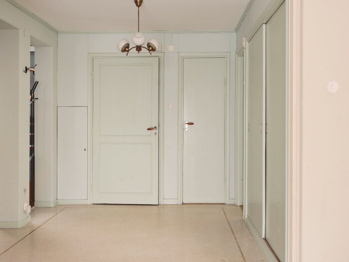 Korridor med ljusgröna dörrar, beige golv, smidesjärn och taklampa i äldre stil.