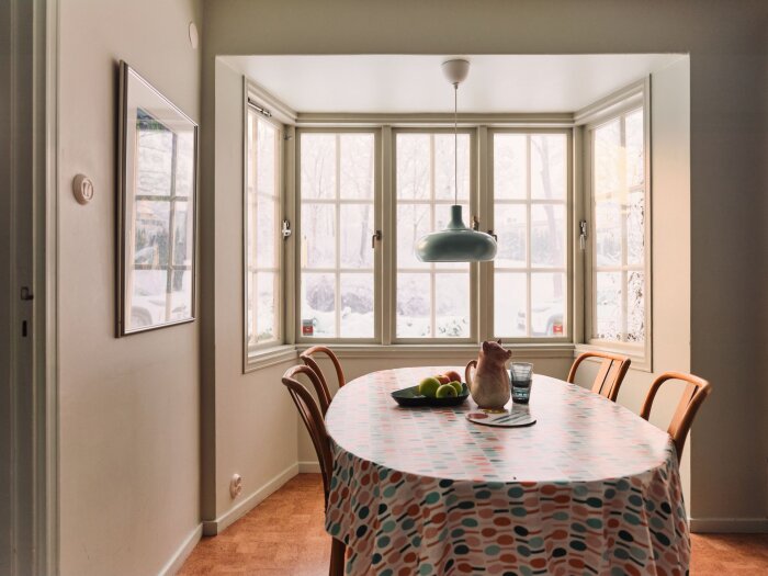Mysigt kök med bord, stolar, fönster utsikt, frukt, karaff och spegel.