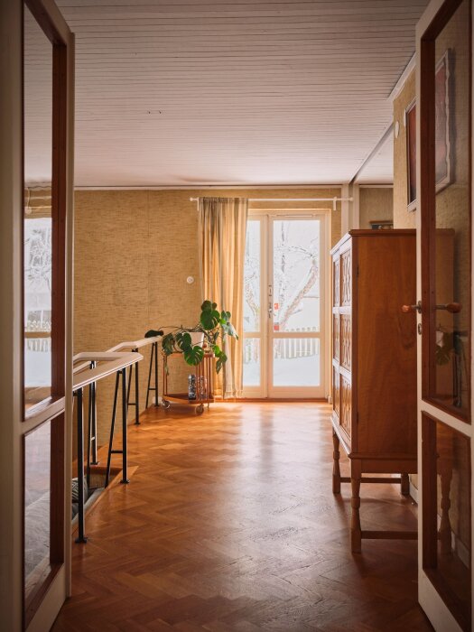 Ett varmt, inbjudande rum med trägolv, möbler, växter och synligt dagsljus från ett fönster.