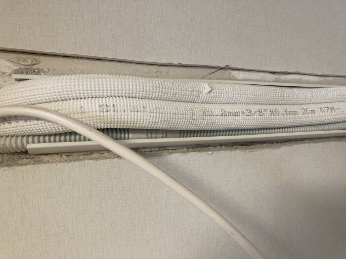 Vit kabelkanal på vägg döljer kablar, elektrisk ledning synlig, vit sladd överst, bakgrundsstruktur av tapet.