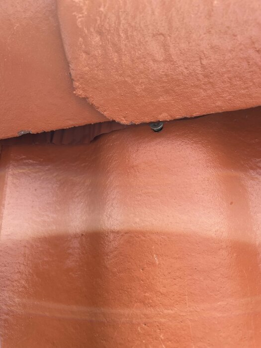 Orange färgade ytor med textur, skiktad, med synlig skruv. Skuggor tyder på ojämn yta.