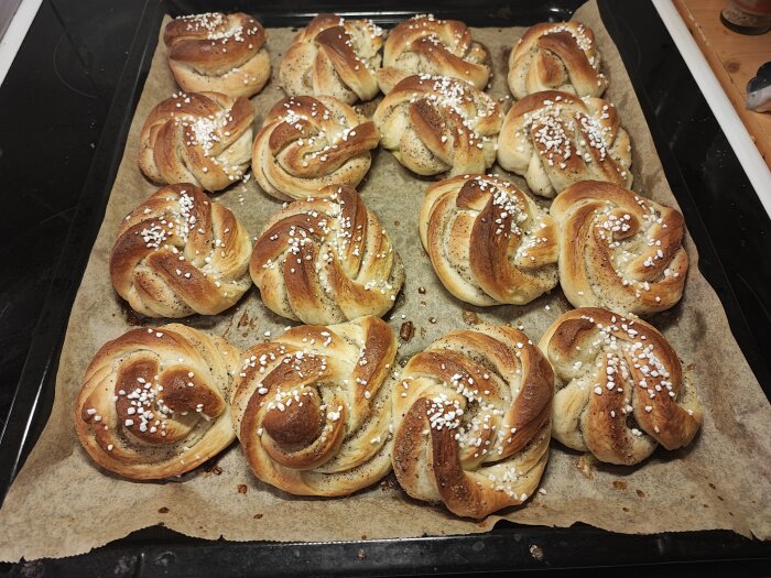 Nybakade kanelbullar med pärlsocker på en ugnsplåt, ser gyllene och läckra ut.