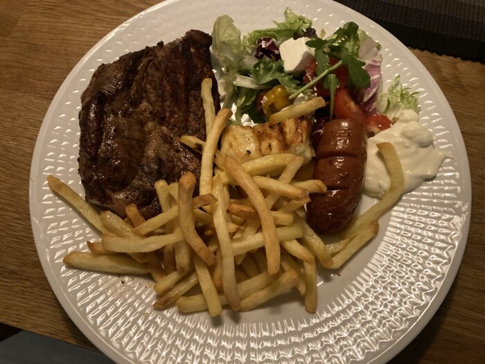 Grillad biff, pommes frites, korv, kycklingbitar, sallad och dippsås på en tallrik.