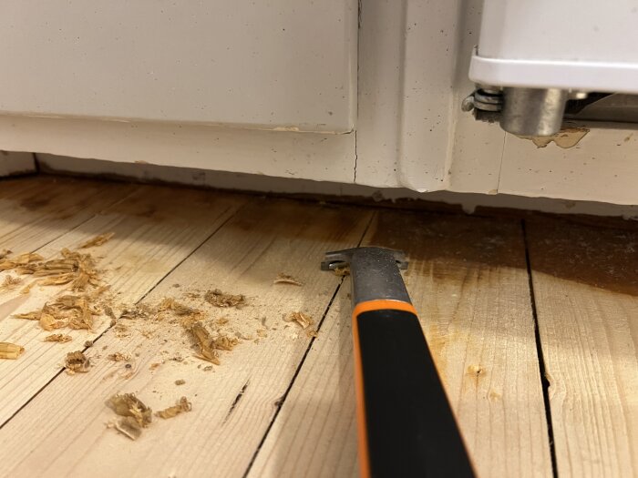 Mejsel på trägolv, spån, vit list, värmerör. Förmodligen renovering eller reparation pågår.