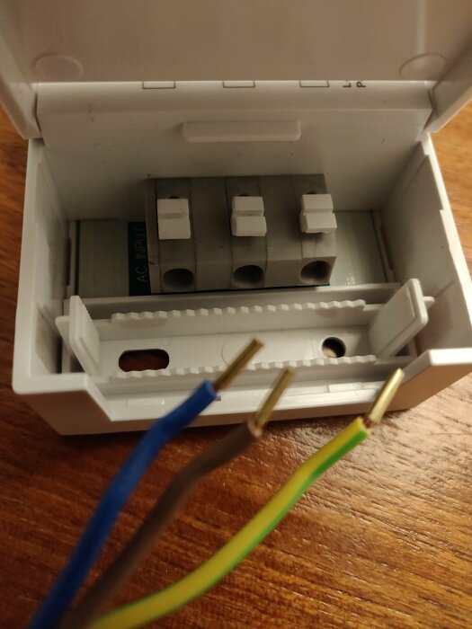 Öppen elektrisk kopplingslåda med tre färgade kablar redo för anslutning: blå, brun, och gul/grön.