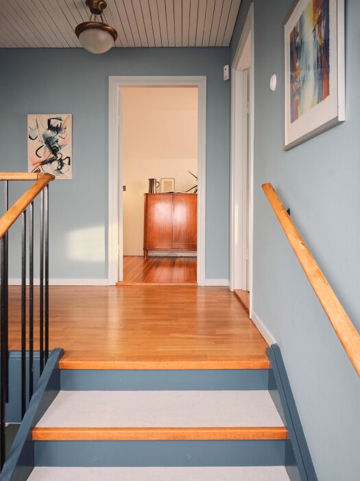 Inomhus trappa, trägolv, blå väggar, konstverk, vit tak, dörröppning, retro inredning, hemmiljö.