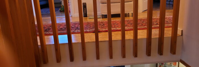 Träspjälor som staket. Inredning syns. Orientalisk matta, del av soffa, leksaker i bakgrunden. Warm indoor lighting.