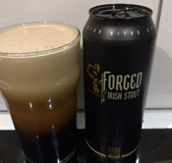 Ölglas med mörkt skummande öl bredvid en stoutburk med text och logotyp.