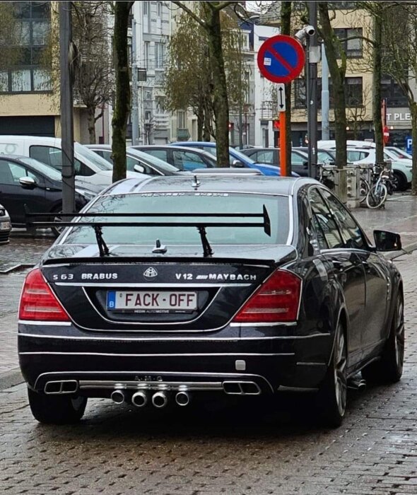 Svart lyxbil parkerad olagligt, intressant registreringsskylt, våt gata, parkerade bilar, träd, stadsområde.