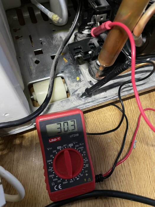 Multimeter som visar 30.3 volt, används för att mäta elektriska komponenter inne i ett skåp.
