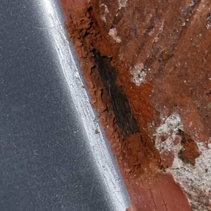 Närbild på en gammal röd tegelvägg vid en metallstruktur med slitage och möjlig fuktskada.