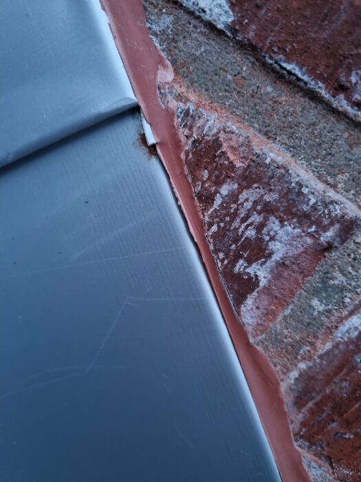 Grå yta möter tegel, med brun tätning, nära detaljbild, möjlig byggnadsstruktur, vinklad perspektiv.