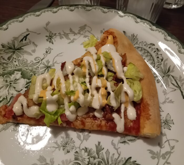 En pizzabit med sallad och sås på dekorerad tallrik.