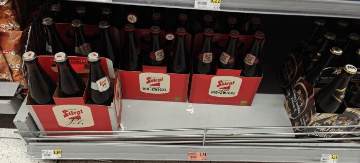 Flaskor av Stiegl Bio-Zwickl-öl i röda förpackningar på en hylla i butik. Prislappar synliga framför.