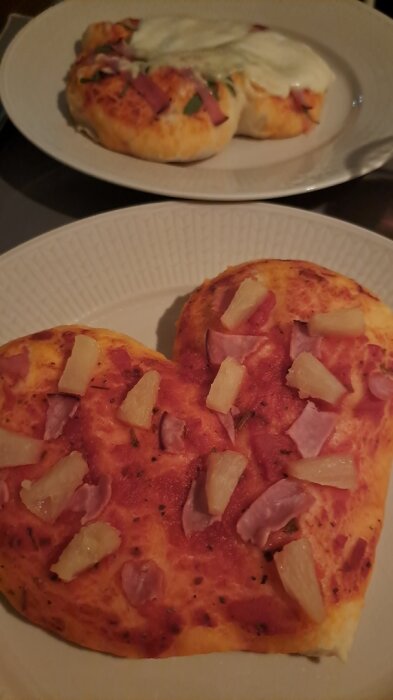 Två pizzastycken på tallrikar; en med ananas och skinka, den andra med grädde och grönsaker.