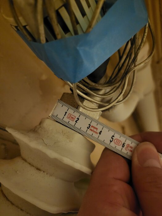 Mätning av en gipsdetalj med måttband, kablar och tejp i bakgrunden.