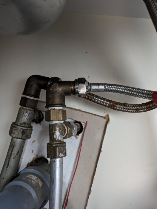 En närbild på vattenrör och anslutningar under en handfat. Olika material, slitage synligt.