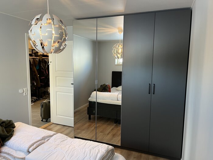 Modernt sovrum med säng, garderobsspegel, snygg taklampa och öppen garderob med kläder.