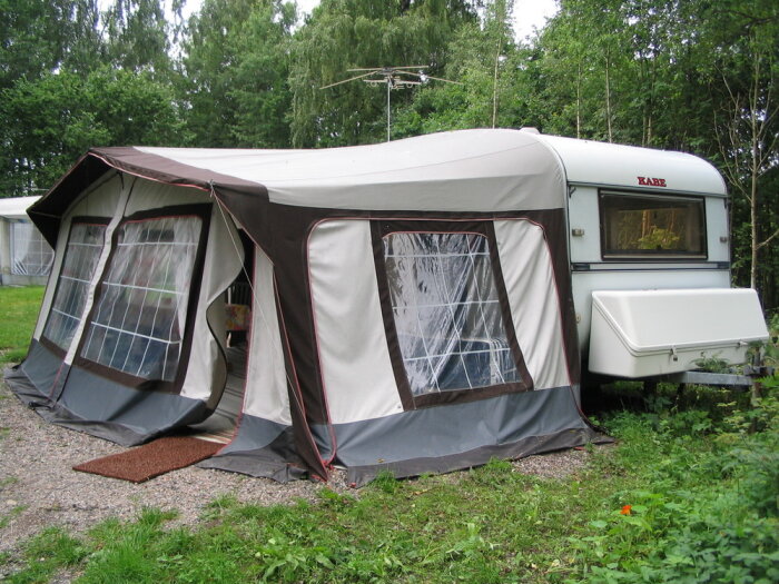 Husvagn med förtält på en campingplats, inbäddad i grönska, somrig fritidsstämning.