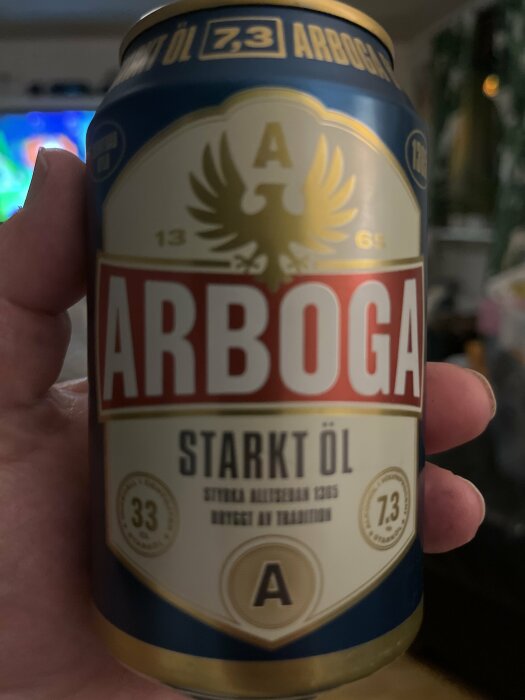 En burk Arboga Starkt Öl, 7.3% alkohol, hålls upp framför suddig bakgrund.