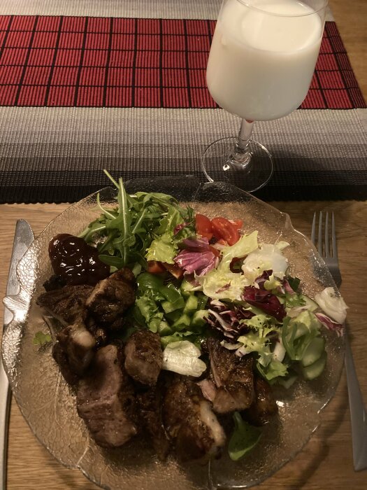 Middag med grillat kött, sallad, barbecuesås och ett glas mjölk.