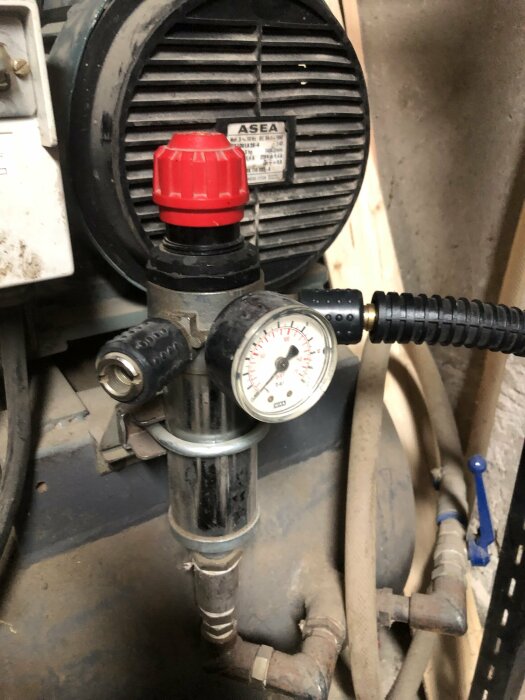 Industriell installation med tryckmätare, rör, svart motor och röda detaljer, troligen en del av maskineri.