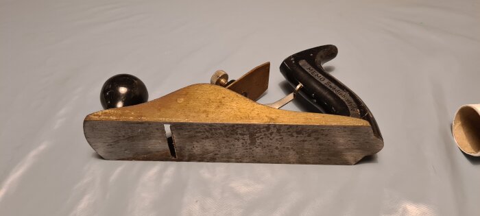 Ett gammalt handverktyg, trähyvel med träknopp och svart handtag, använd för slätning av trä.