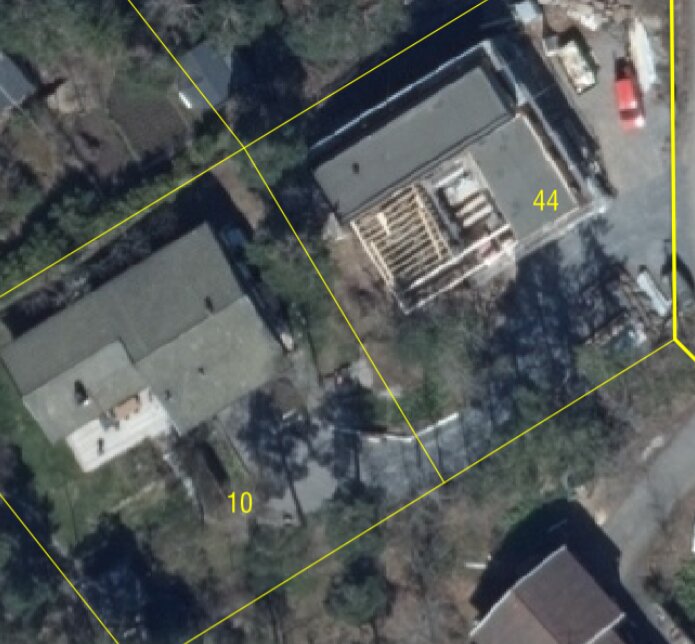 Satellitbild över bostadsområde med byggnader och pågående konstruktion. Gator och träd syns även.