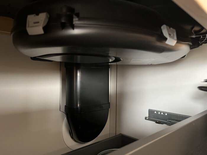 Bild på en kaffemaskin under ett köksskåp, möjligtvis en inbyggd modell, fotograferad från en låg vinkel.