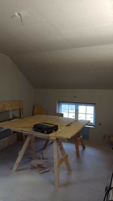 Oavslutat rum under konstruktion med träbänk, verktygslåda och synliga isoleringsskivor på väggarna.