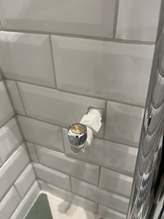 Toalettpapper på hållare med liten bit kvar, vita kakelväggar, grön duschmatta skymtar.