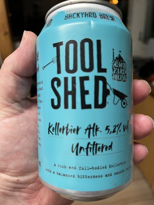 En hand håller en ölburk med texten "TOOL SHED", "Kellerbier Alk. 5,2% vol." och "Unfiltered".