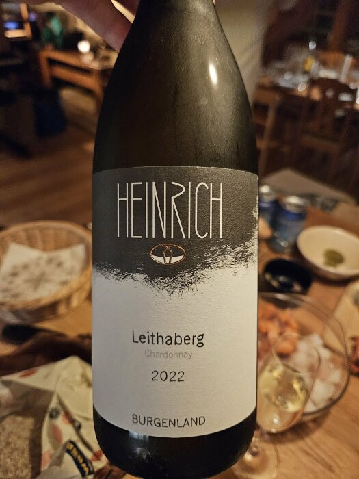 Vinflaska märkt "HEINRICH", "Leithaberg Chardonnay 2022", BURGENLAND, i diffust upplyst inomhusmiljö.