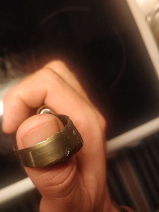 En hand håller ett brutet föremål, troligen ring eller metallband, nära kameran med suddig bakgrund.