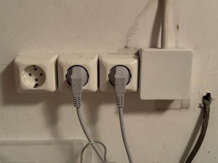 Vit vägg med flera eluttag och kablar, en är oanvänd, och en Schneider-enhet.