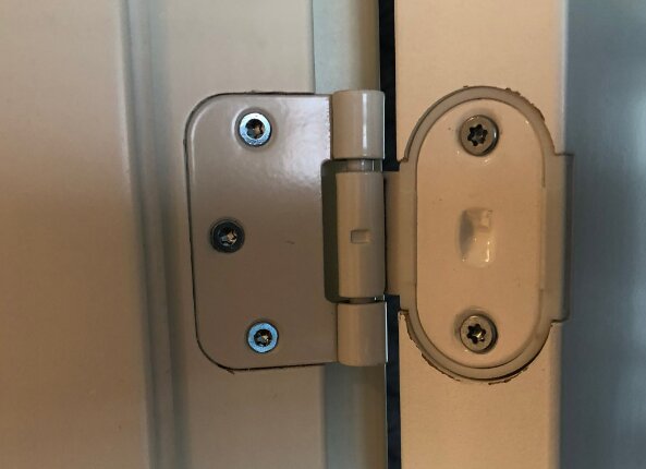Metallisk dörrstängare med skruvar på en vit dörrkarm, inomhus.