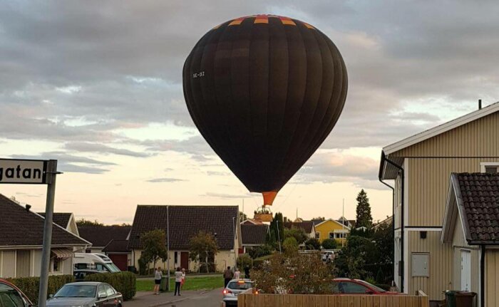 En varmluftsballong landar nära bostadshus, med åskådare, vid skymningen.