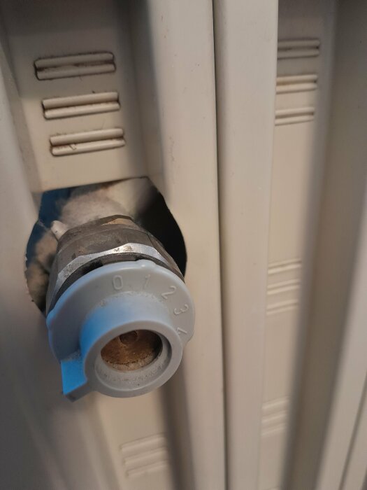 Termostatventil på en radiator, inställningar 0-5, delvis dammig, vit och blå detaljer.