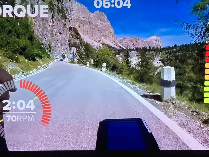 Bild av en interaktiv träningscykelskärm som visar en slingrande väg genom ett bergigt landskap.