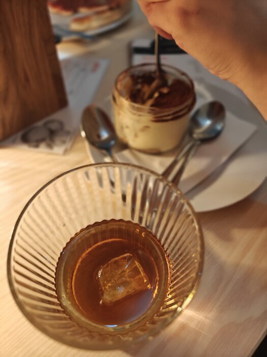 Ett glas med troligen whisky och is bredvid en dessert som äts. Oskarpa objekt och varma färgtoner i bakgrunden.