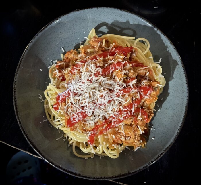 Spaghetti med köttsås och riven ost på grå tallrik.