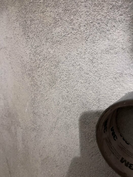 Grå texturerad vägg, skugga av en person, brun rulle i nedre högra hörnet.