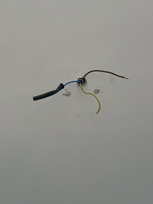 Eluttag under installation med oskyddade, färgkodade elektiska kablar på en vit vägg.